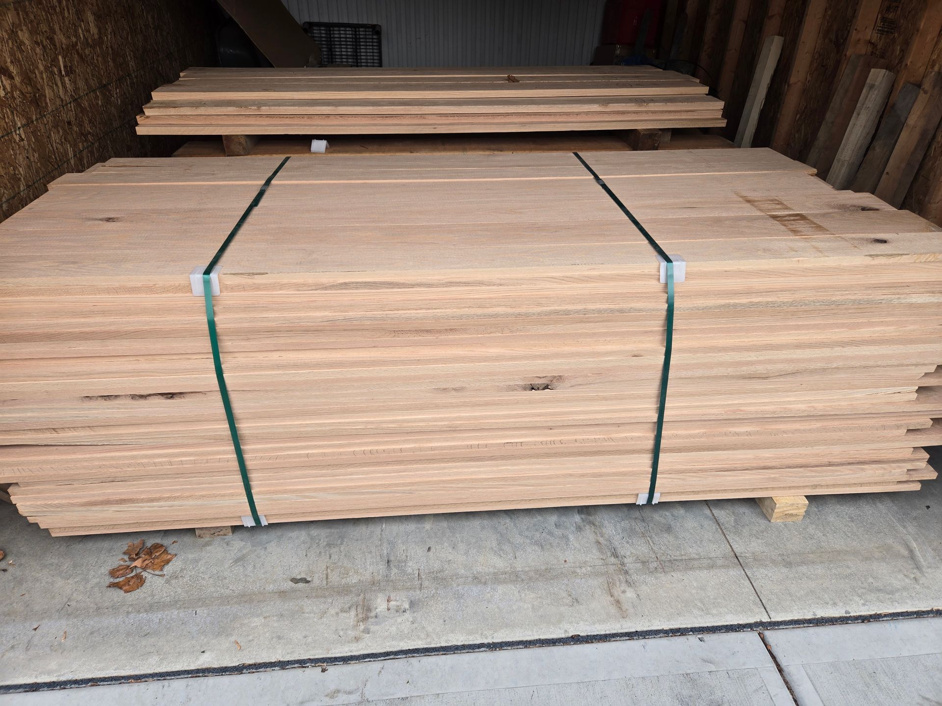Two stacks of unfinished, light-colored wooden boards are bundled together on a concrete floor in a storage area.