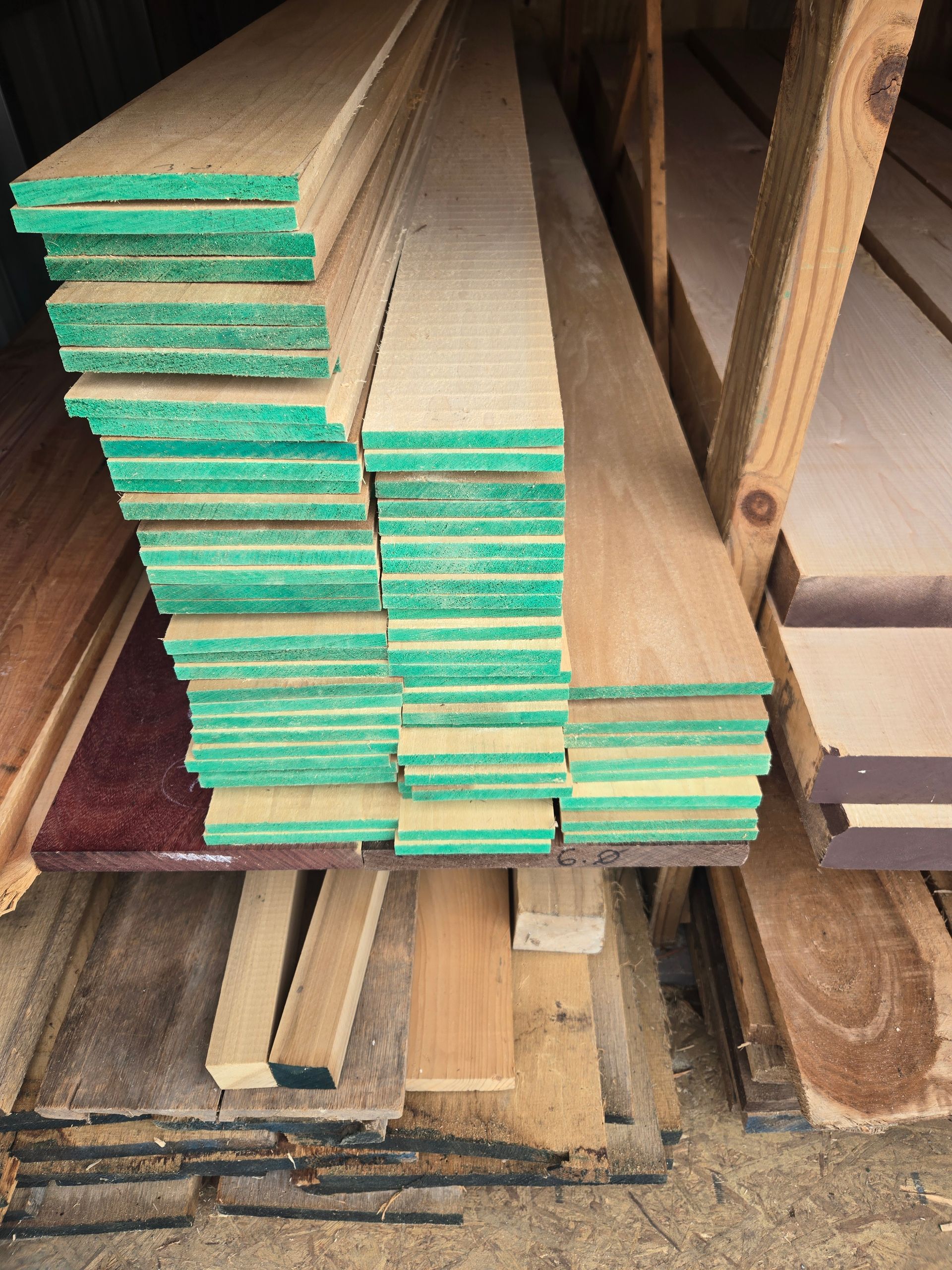 A stack of lumber planks with green-tinted ends, sitting on a wooden storage rack in a workshop or warehouse.