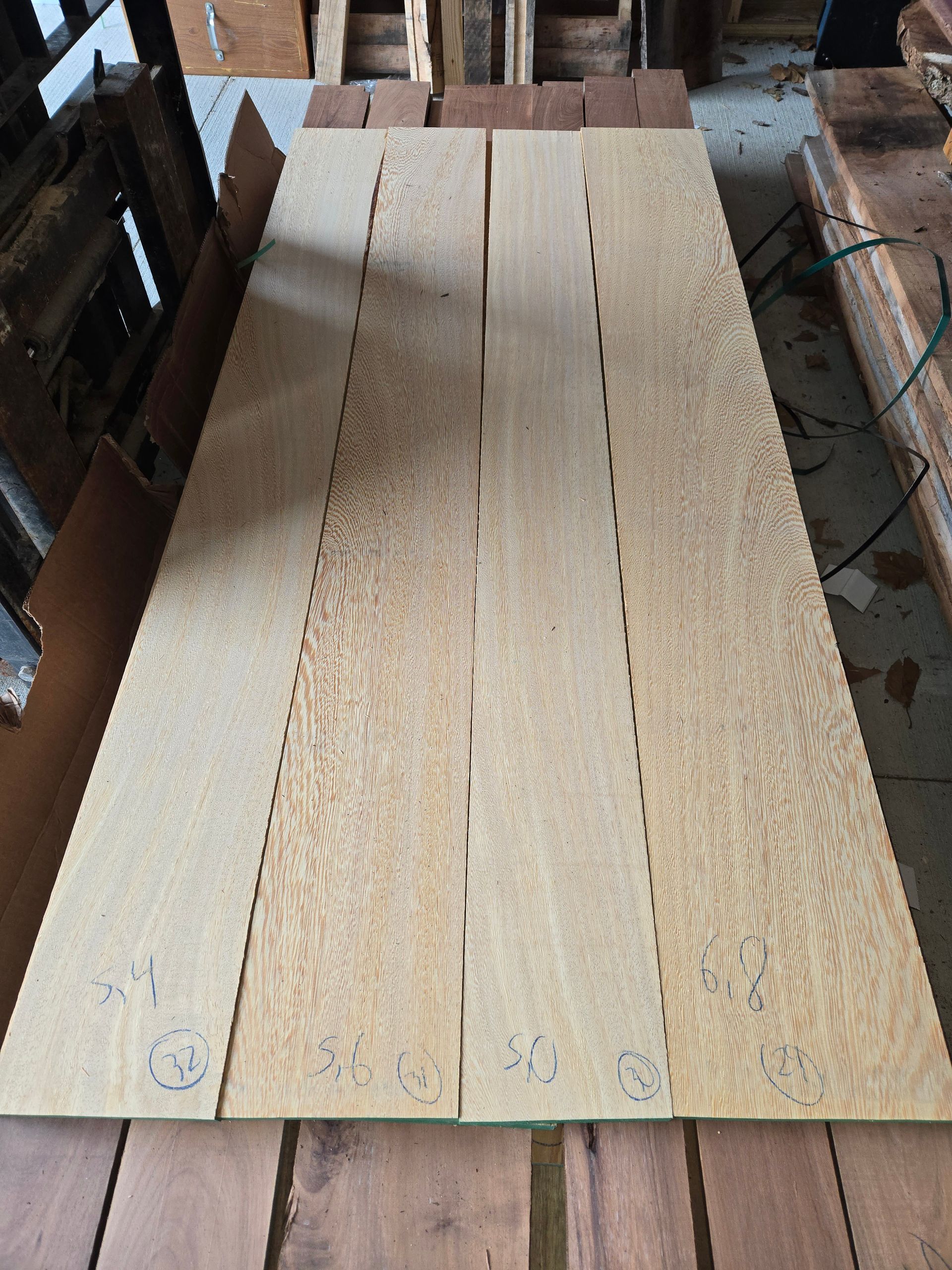 Four light-colored, long wooden boards laid side-by-side in a workshop, marked with numbers at the bottom.