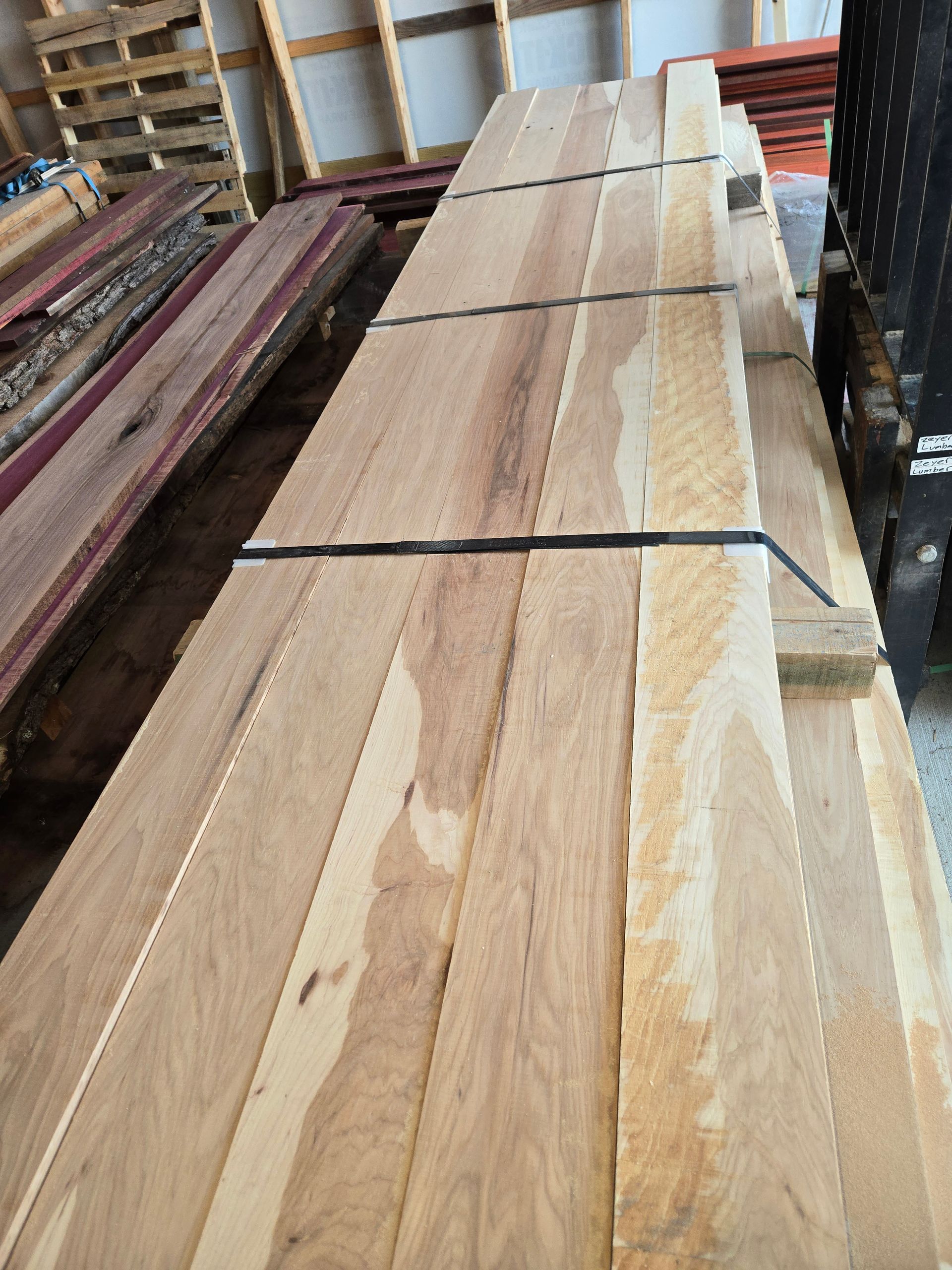A bundle of light-colored, rough-sawn hardwood planks stacked and strapped together in a warehouse setting.