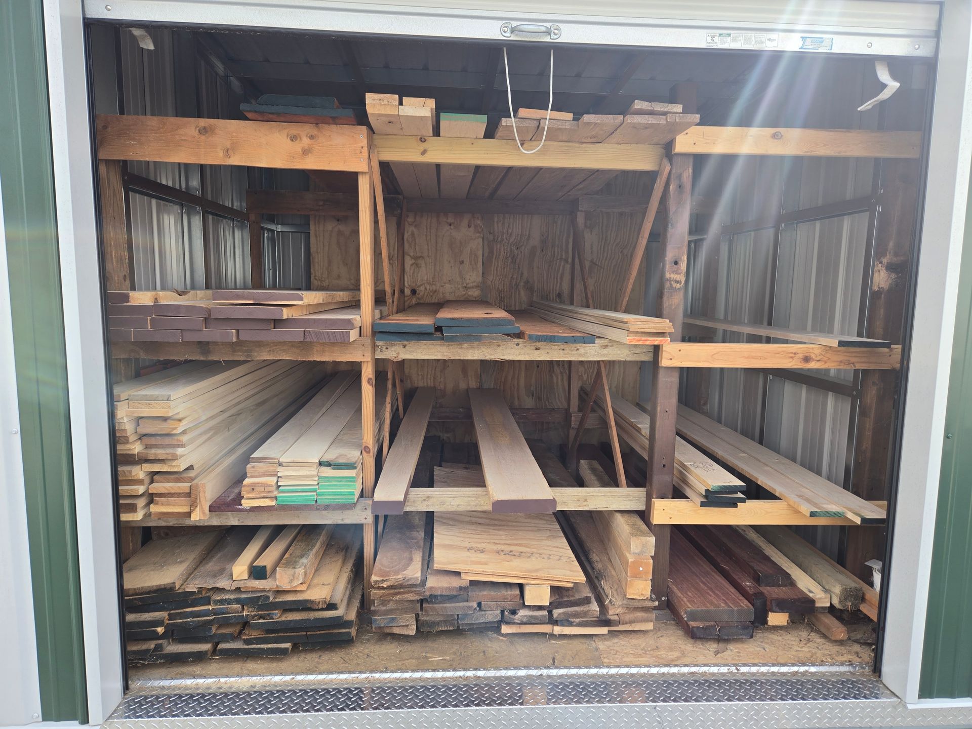 A wooden storage shed filled with stacked lumber on three-tiered shelves.