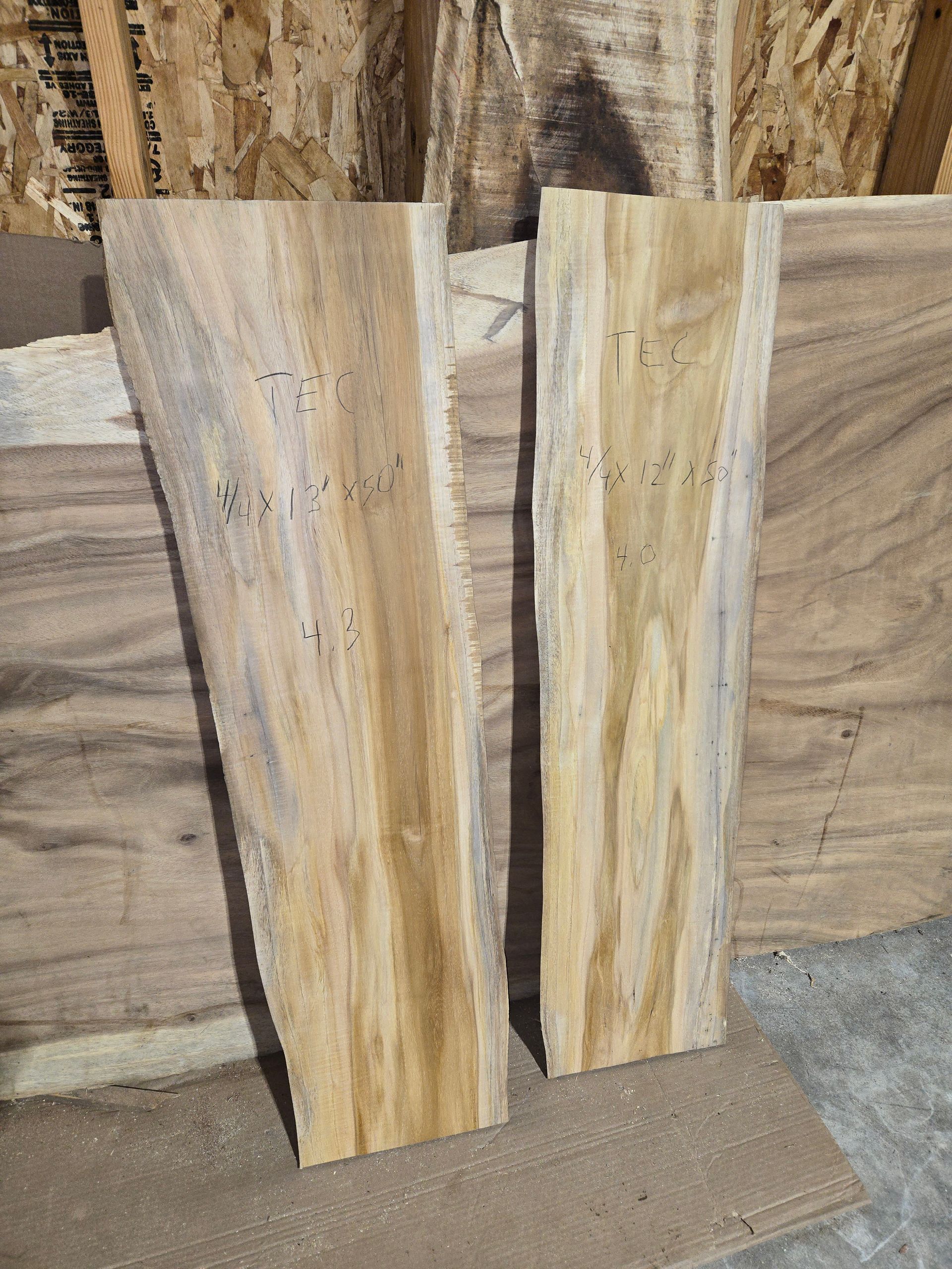 Two vertical slabs of light-colored wood with natural live edges stand side-by-side against a wooden background.