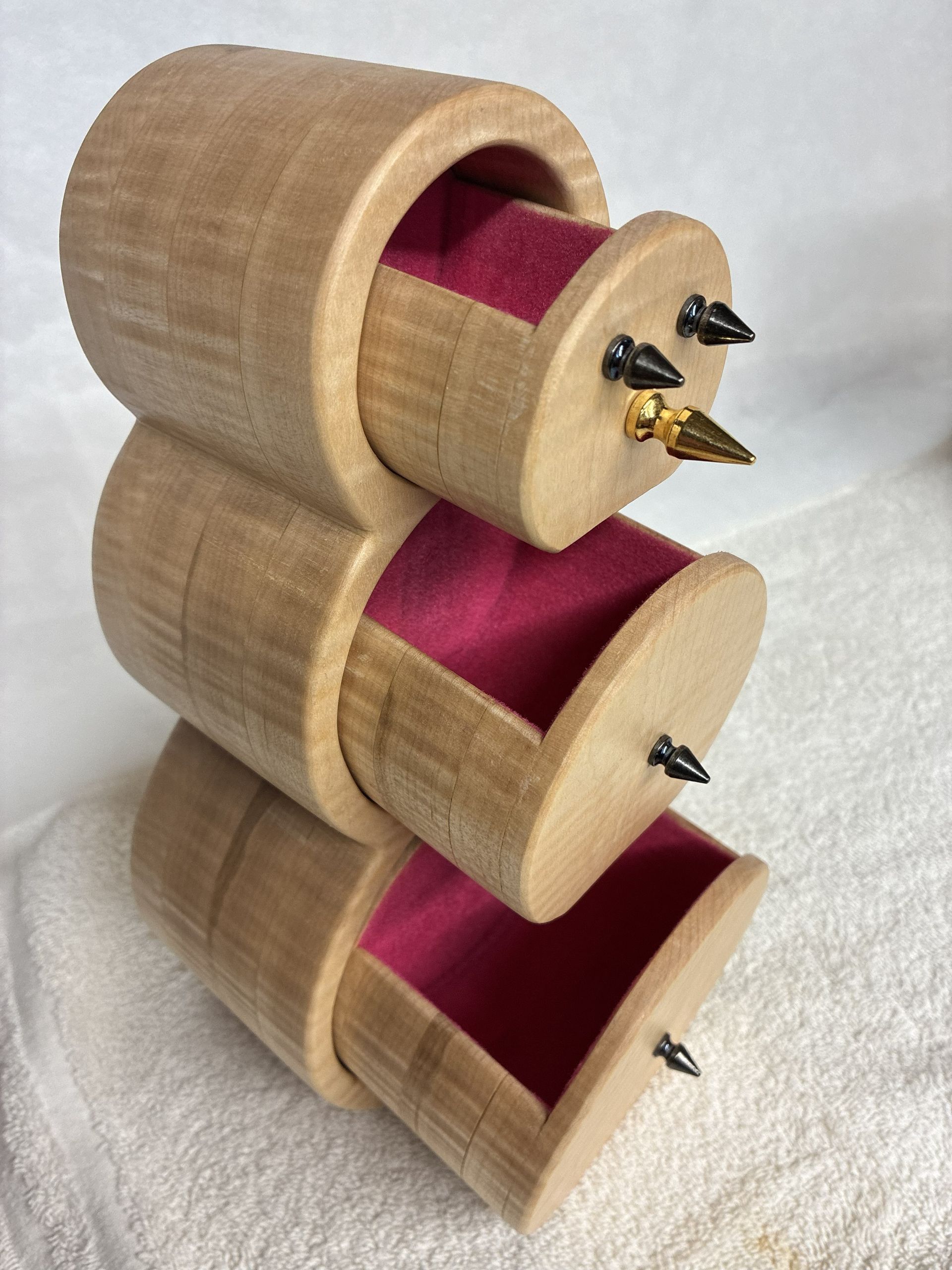 A three-tiered wooden cylindrical jewelry box with drawers lined in pink velvet and accented with small metallic spikes.