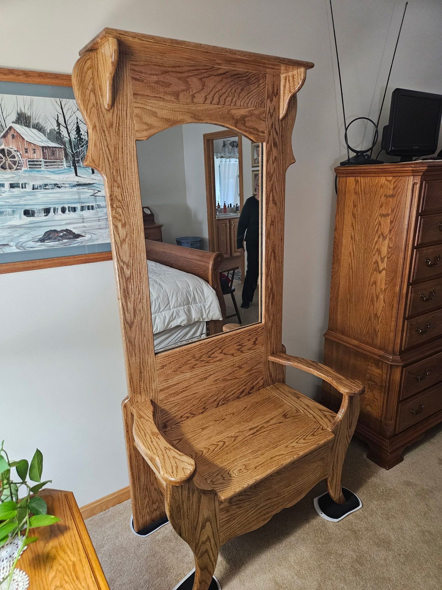 An ornate, medium-oak hall tree with a built-in mirror, storage bench seat, and curved wood trim in a bedroom setting.
