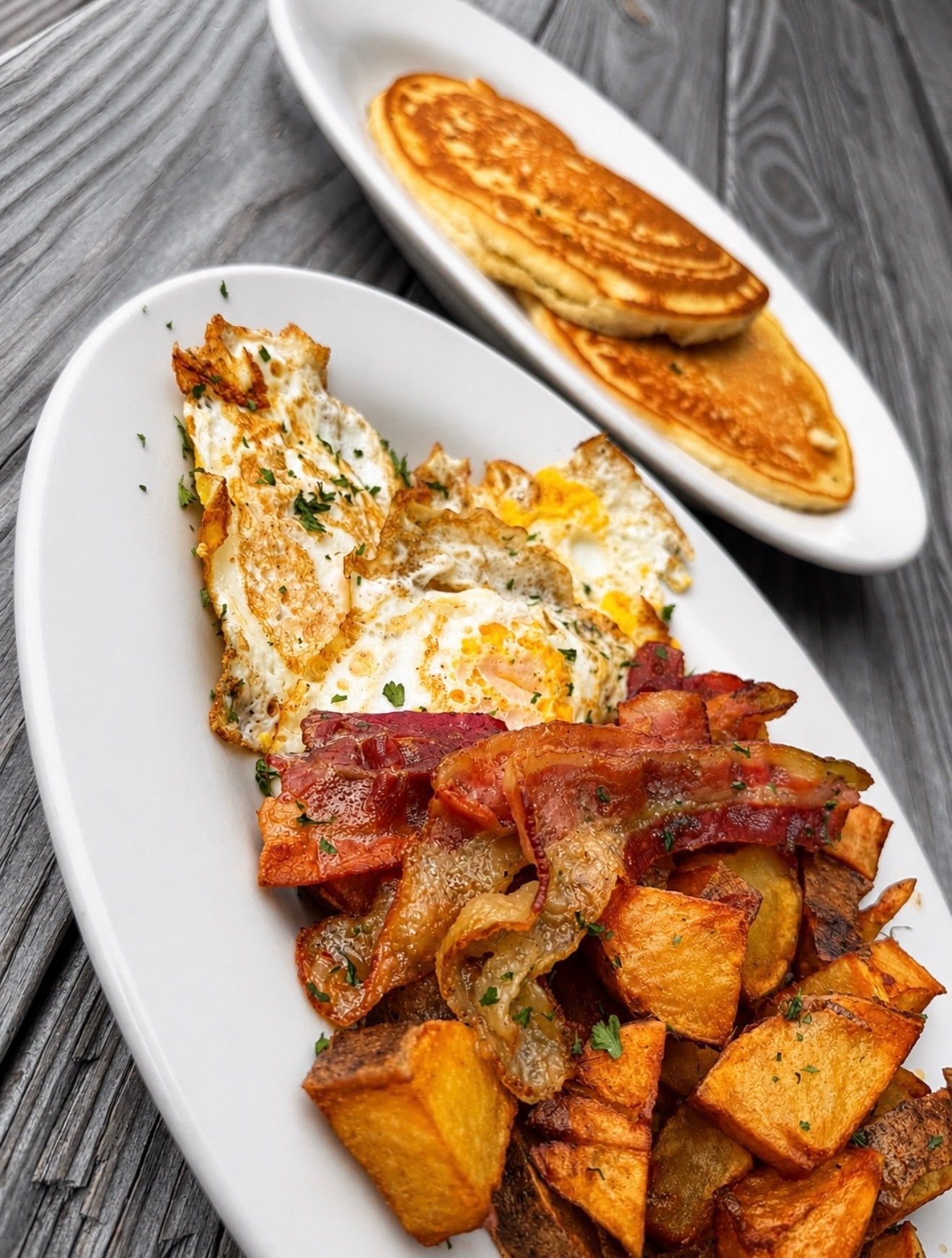 Breakfast plate with fried eggs, bacon, hash browns, and pancakes on a white dish