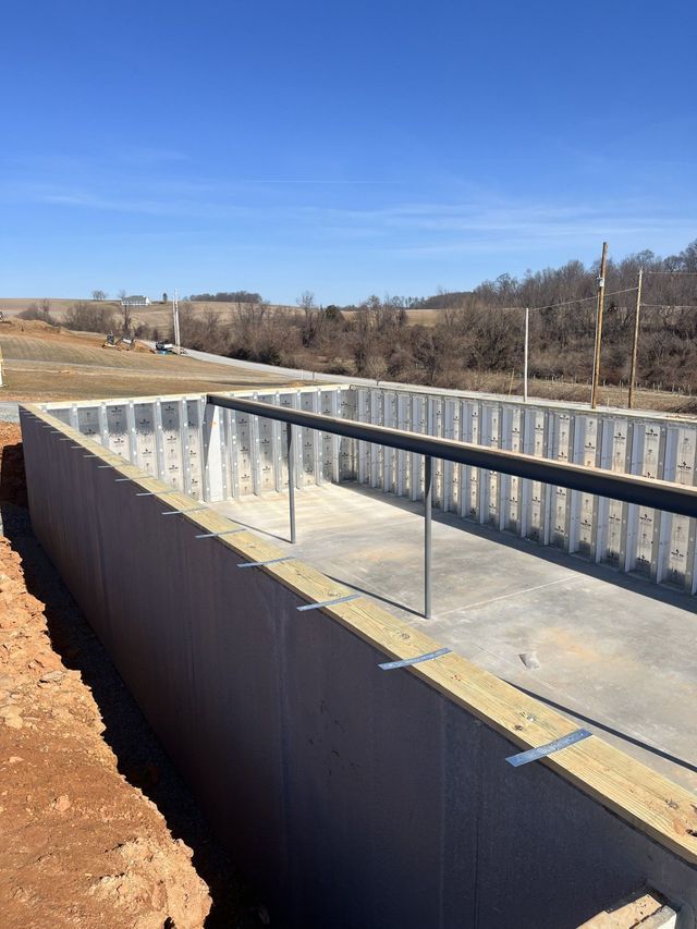 Foundation walls of a rectangular structure under construction, with a black pipe railing on the concrete floor.