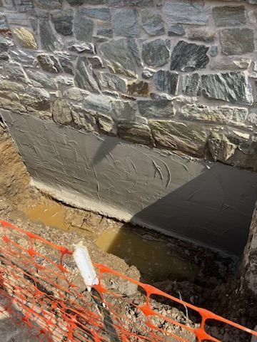 Stone wall foundation under construction, with freshly applied dark coating.