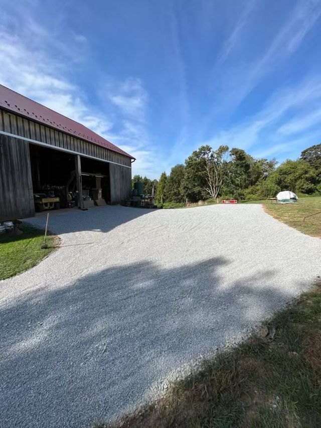 Gravel driveway leading to a weathered barn with a red roof, under a partly cloudy blue sky.