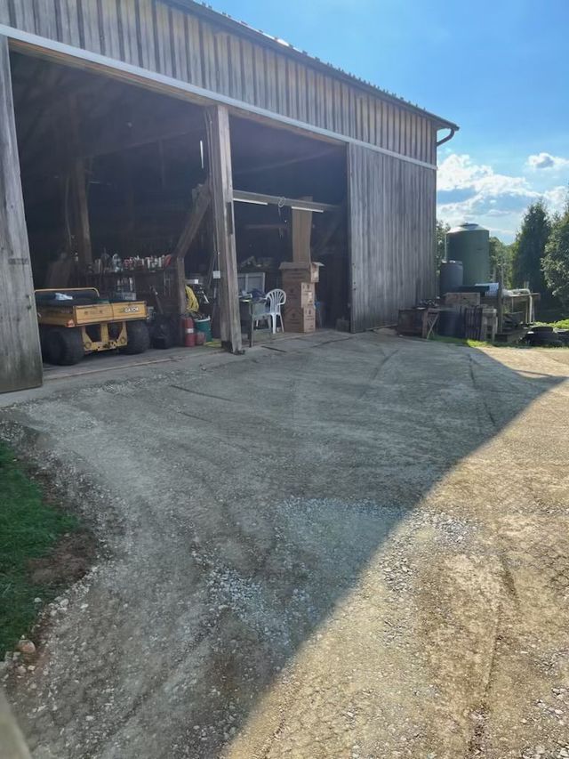 Gravel driveway leading into a weathered wooden barn, sunny day.