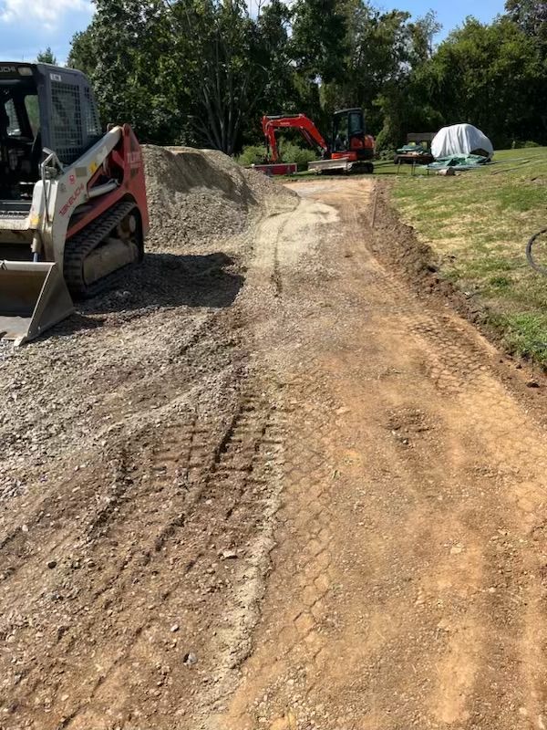 Construction site with a dirt road, gravel pile, and heavy machinery; sunny day.