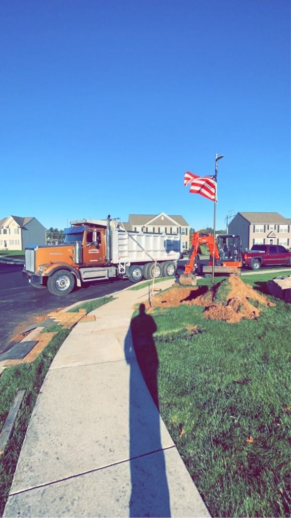 Truck and excavator at a construction site. American flag waves. Sunny day.