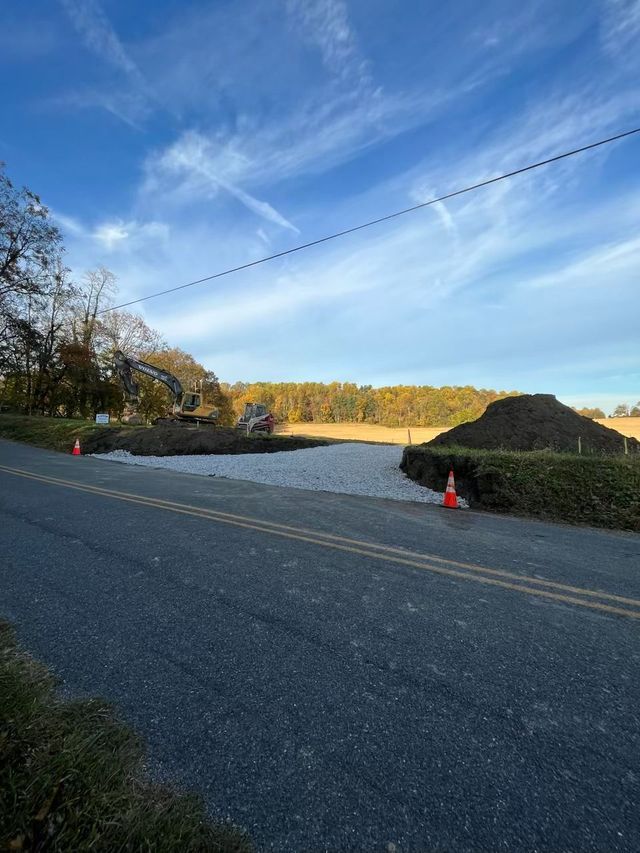 Road leading to construction site with pile of rocks, orange cones, and blue sky.