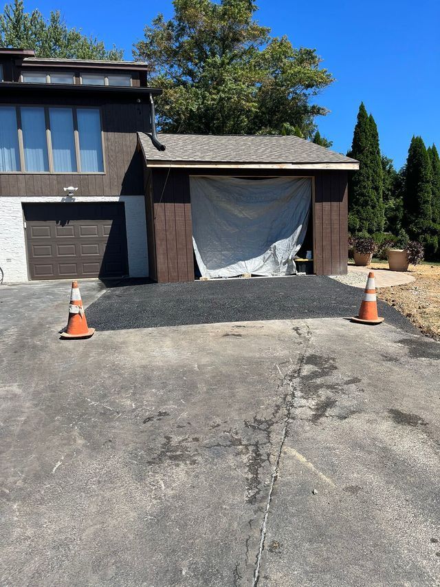 Asphalt and orange cones in front of a house and garage with a tarp covering the opening.