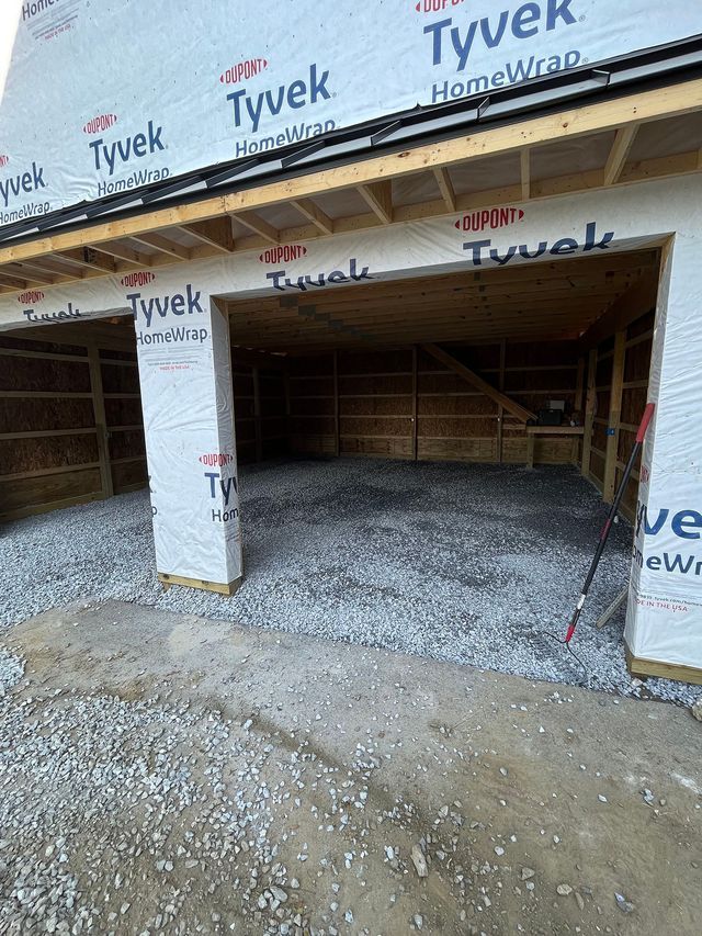 Garage under construction. Gravel floor, Tyvek wrap, wooden beams, open bays.