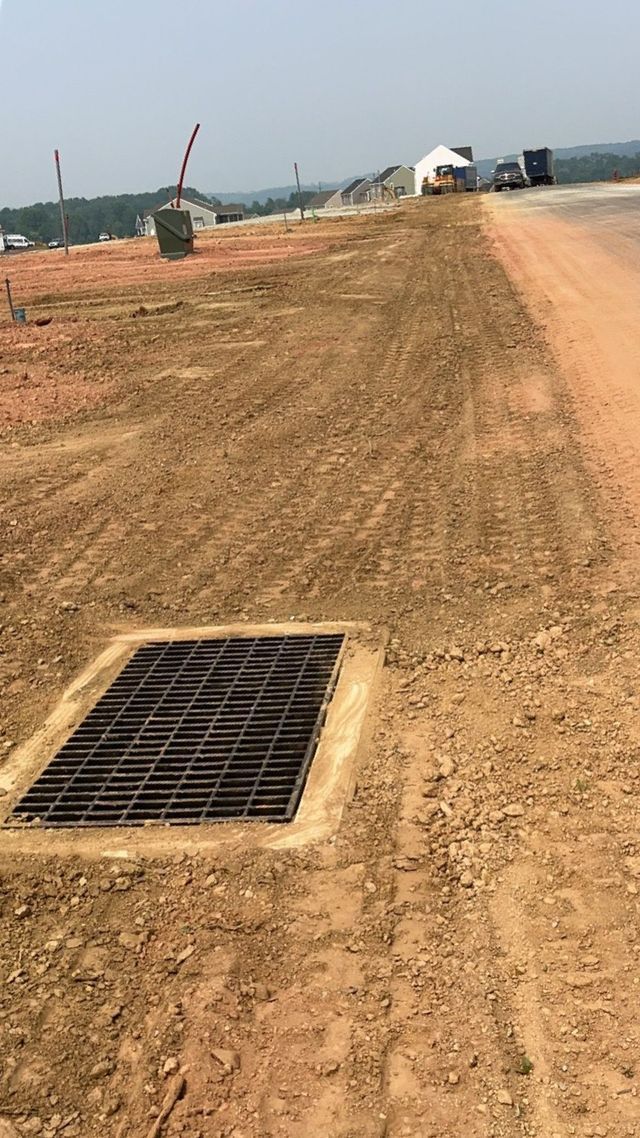 Open drainage grate in dirt road; construction site background.