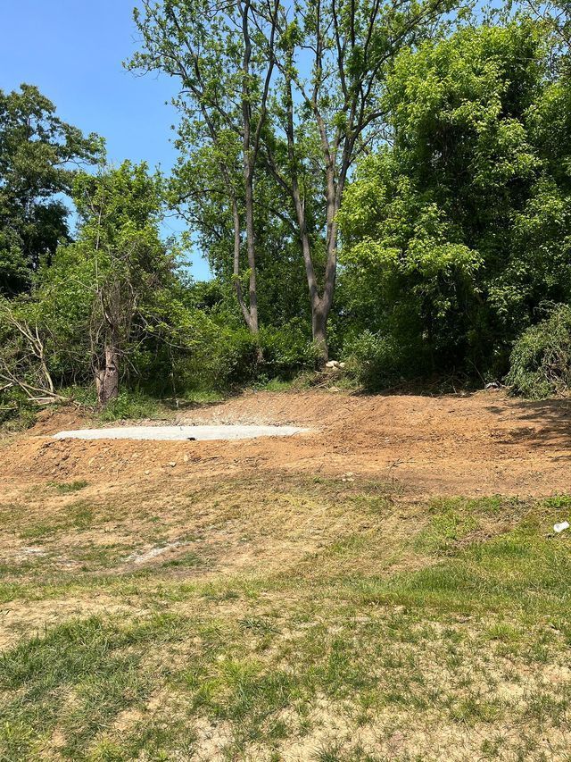 Cleared area of dirt and grass with trees in the background under a blue sky.