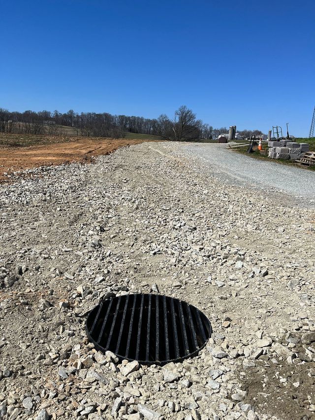 Gravel road with a metal grate in foreground, leading to a blue sky and construction site.
