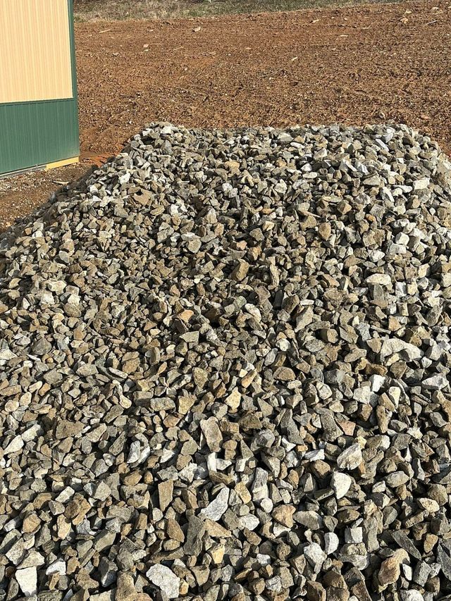 Pile of grey and tan gravel on brown earth near a green and yellow building.