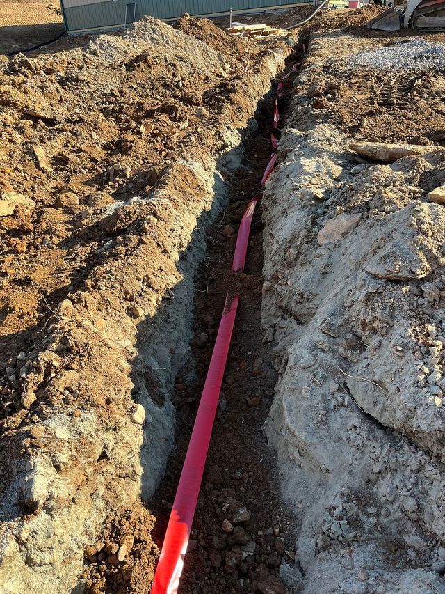 A trench with pink conduits in the ground for electrical or communication lines.