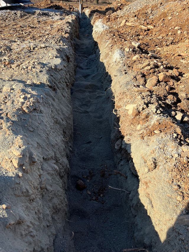 Narrow, excavated trench in dirt, ready for underground installation.