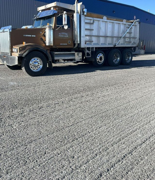 Brown dump truck parked on a gravel surface next to a blue building.