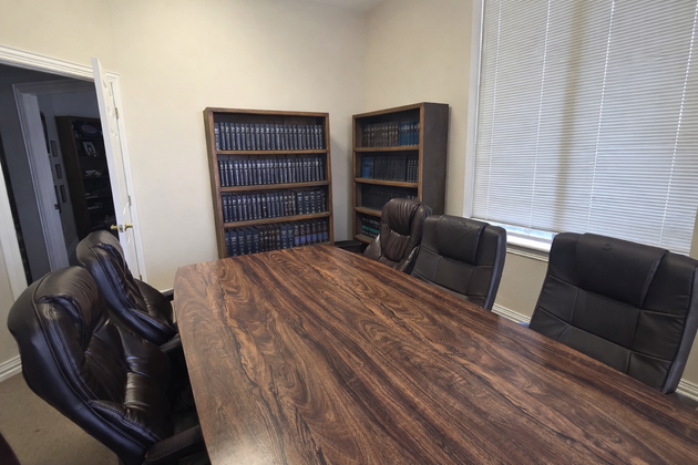 A conference room with a large wooden table, several dark leather office chairs, and two bookshelves filled with binders.