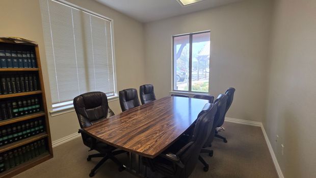 A conference room with a large wooden table, six black chairs, and a tall bookshelf filled with books along the left wall.