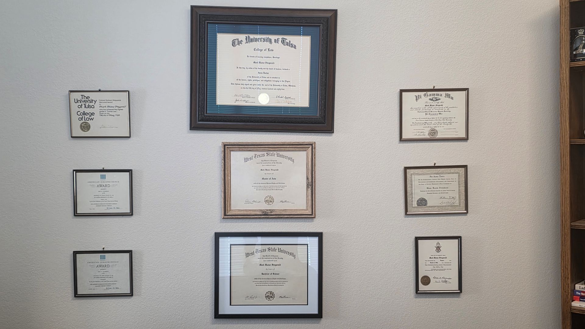A wall display featuring seven framed certificates or awards arranged in three columns on a textured light-colored wall.