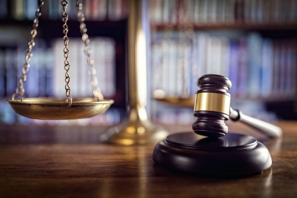 Scales of justice and gavel on a wooden desk, with blurred bookshelves in the background.