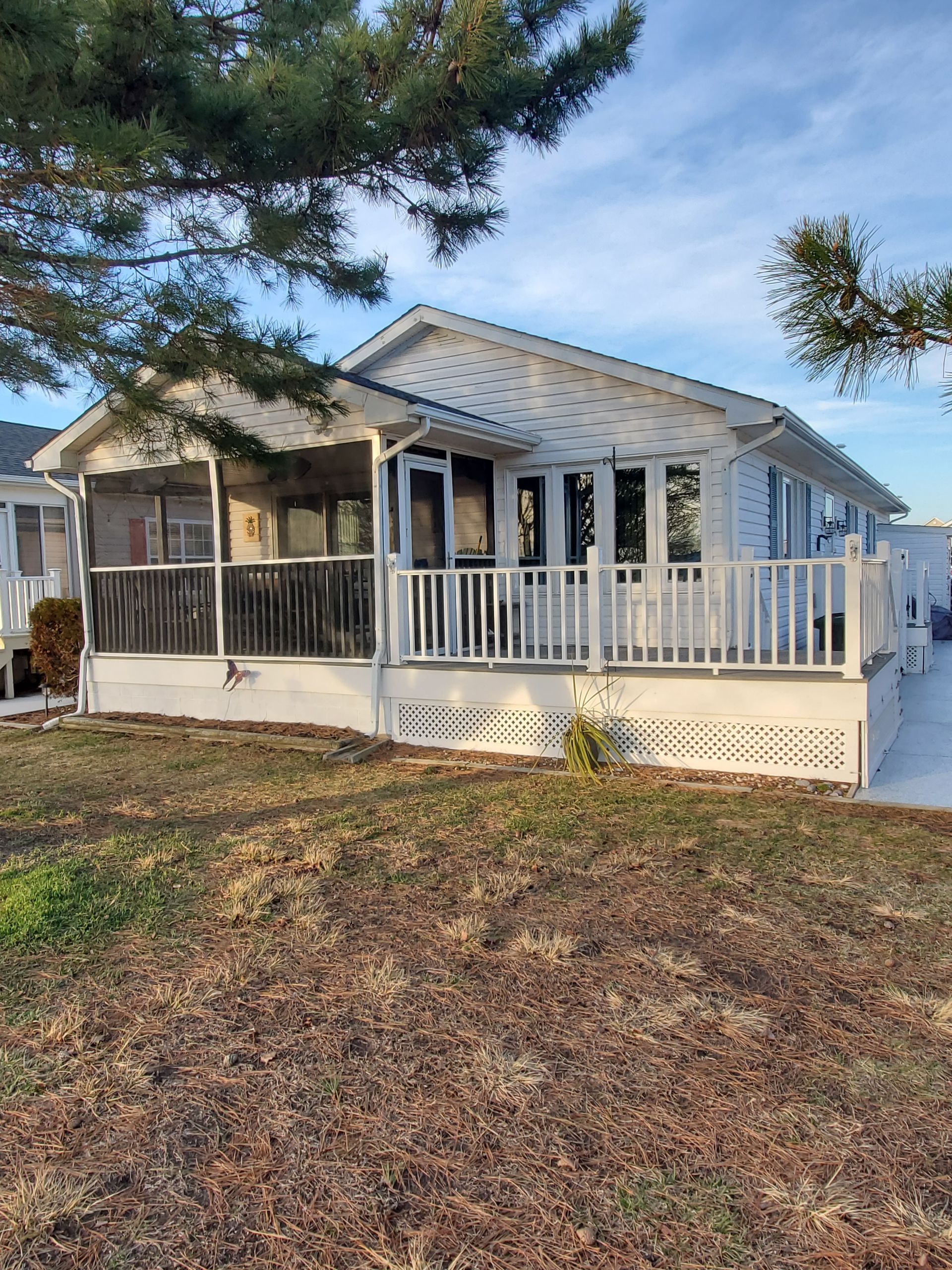 White house with a screened porch and deck, set on brown grass with a blue sky in the background.