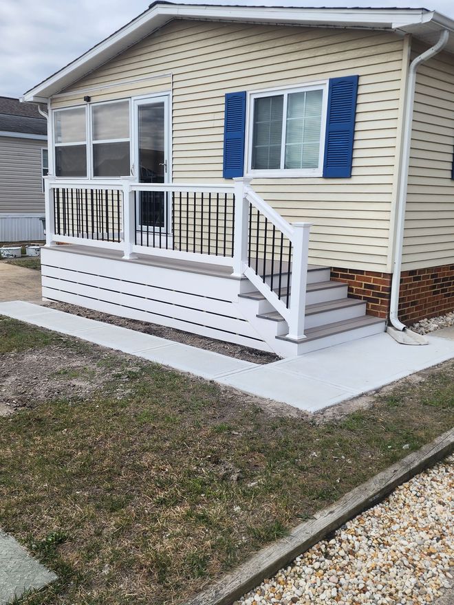 Cozy beige house with a porch. Blue shutters and white railing. Cement walkway leads to the steps.