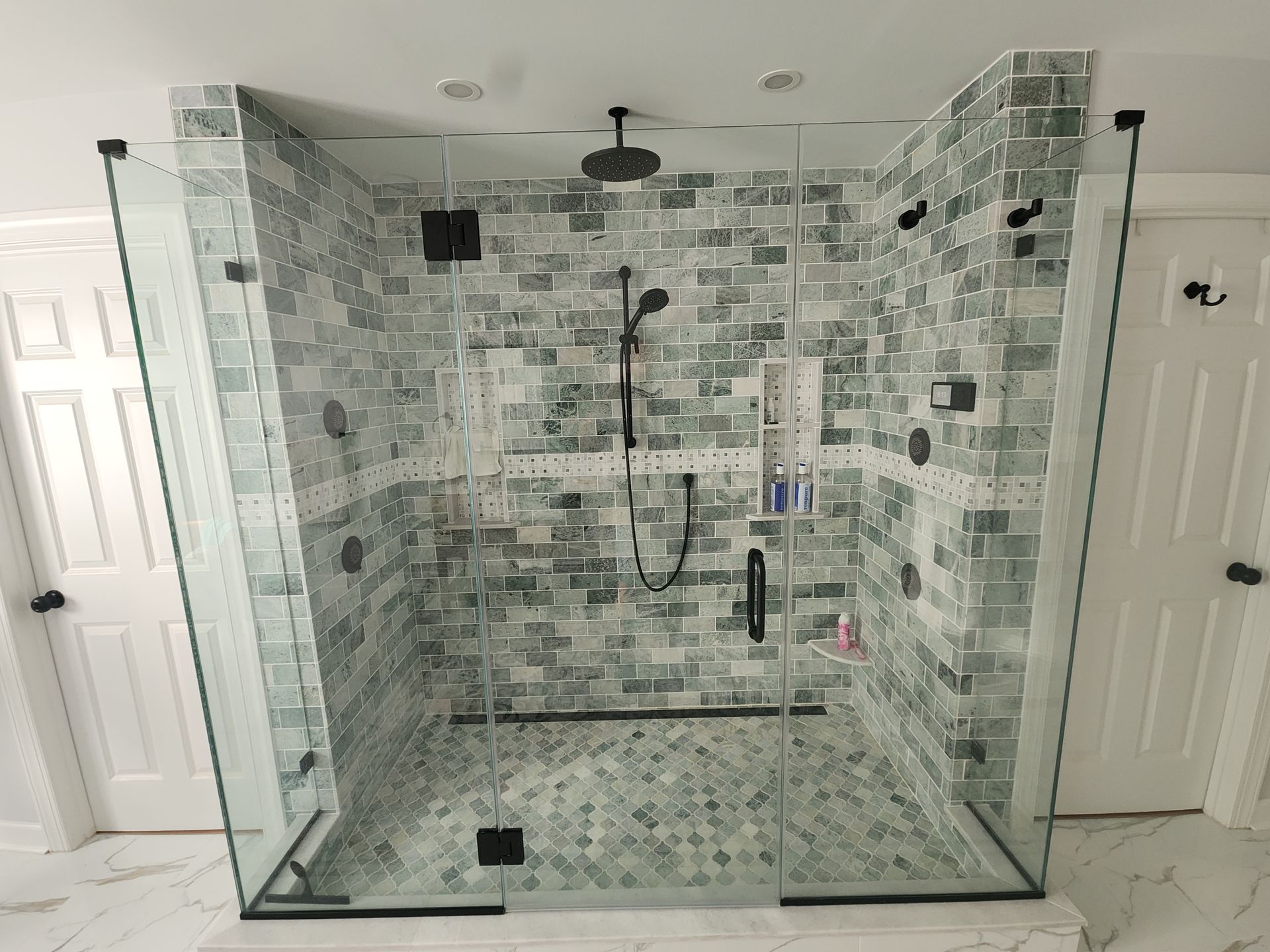 Modern shower with green brick-like tile, multiple shower heads, glass doors, and black fixtures.