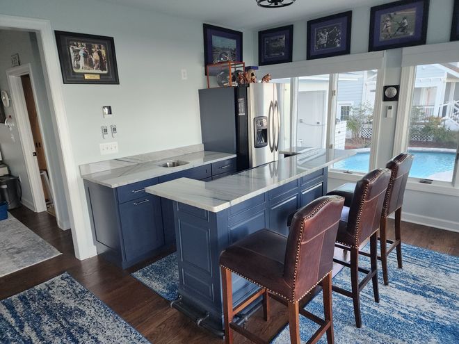 Blue kitchen with island and stools, marble countertops, stainless fridge, and view of a pool.