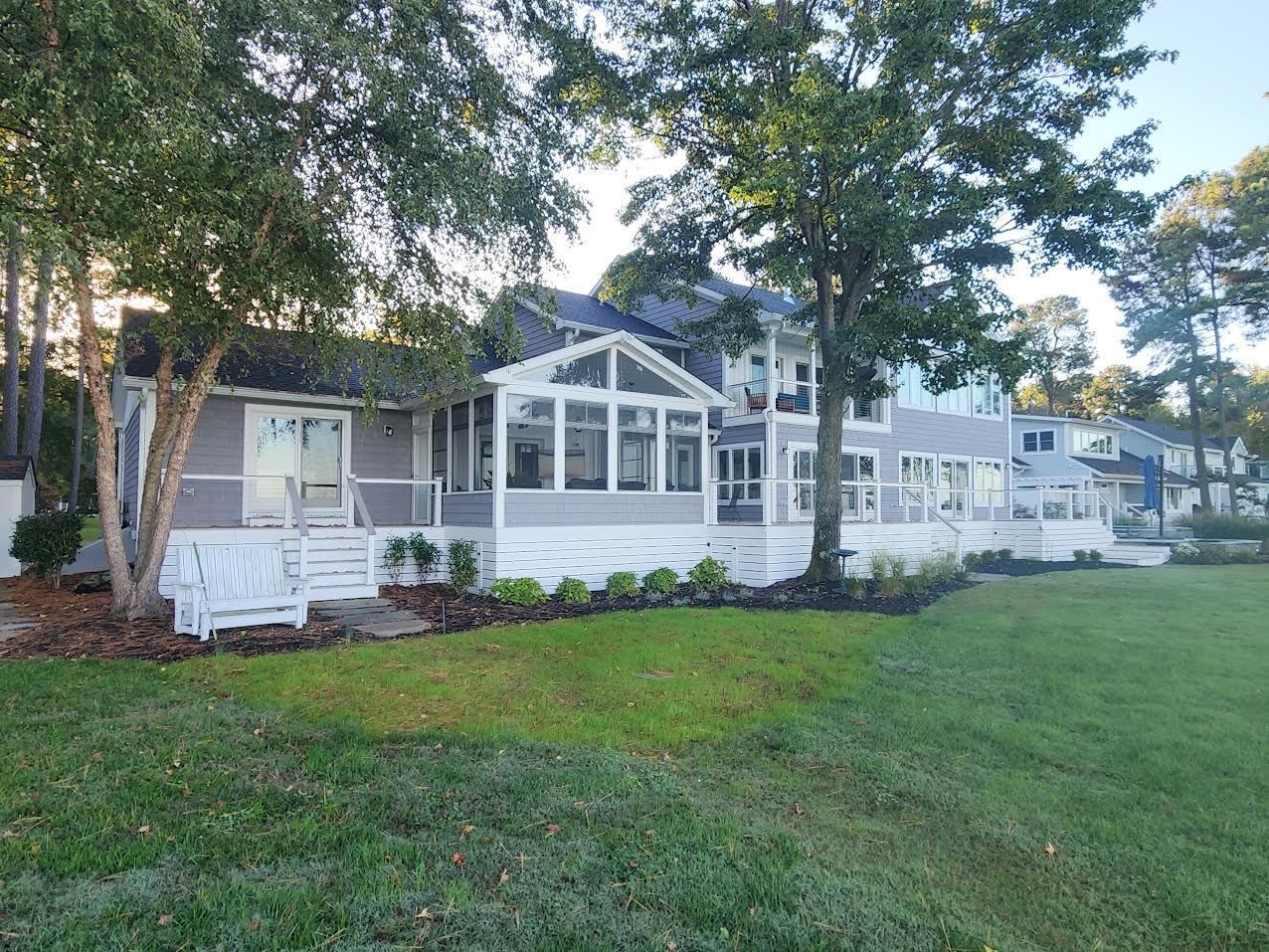 Lakeside house with gray siding, white trim, and a porch, set amongst trees on a grassy lawn.