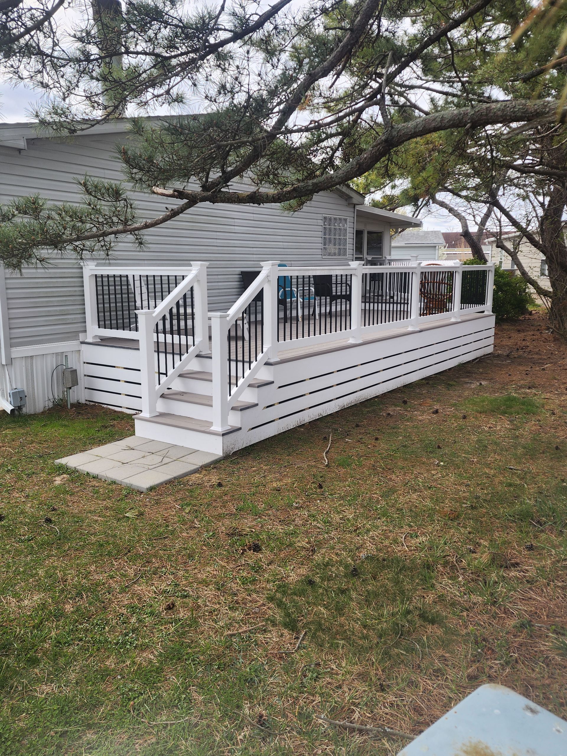 White deck with stairs, black railing, attached to a light-colored house. Outdoor setting with grass and tree.