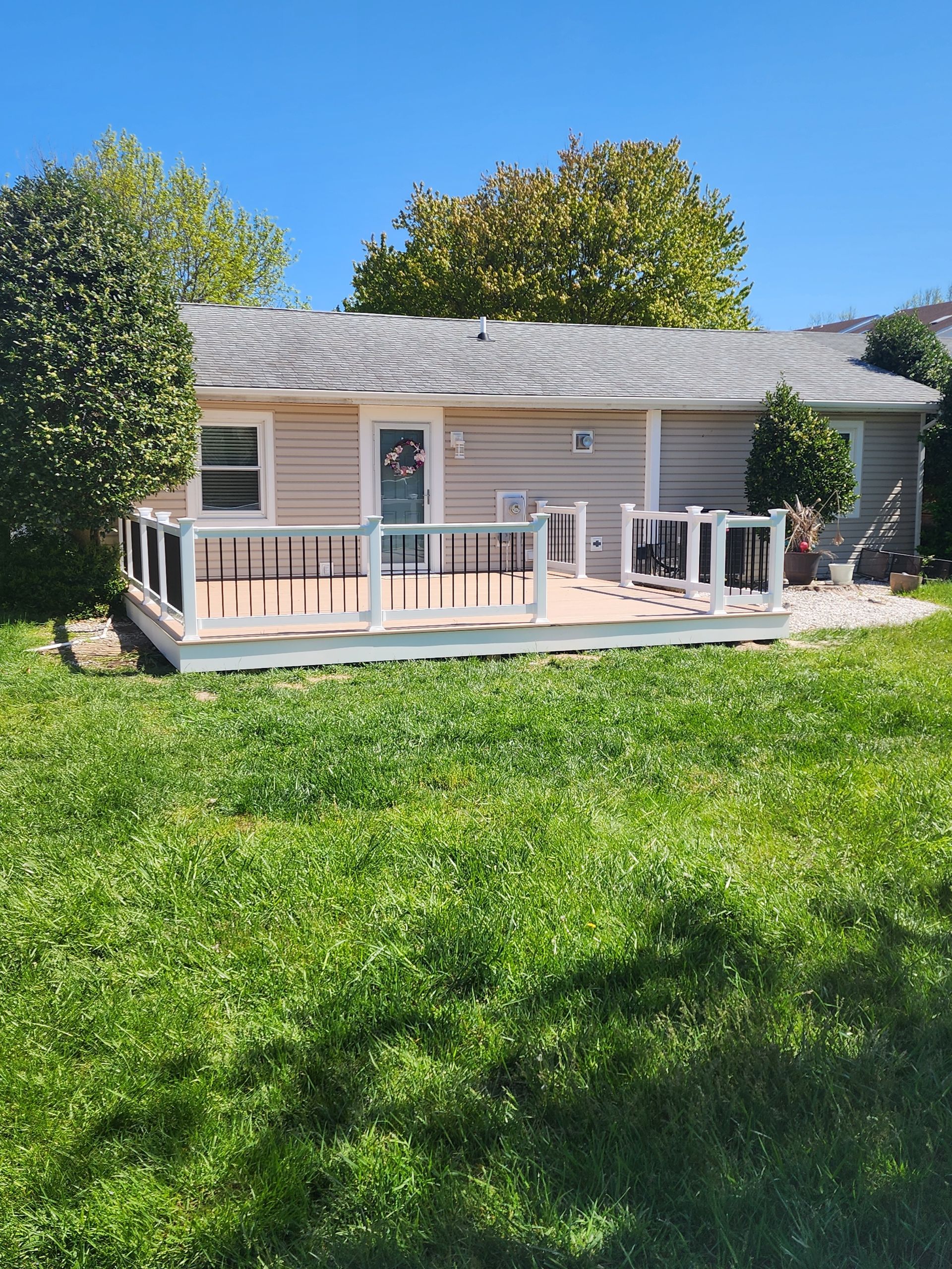 Backyard view of a house with a wooden deck, surrounded by green grass and trees.