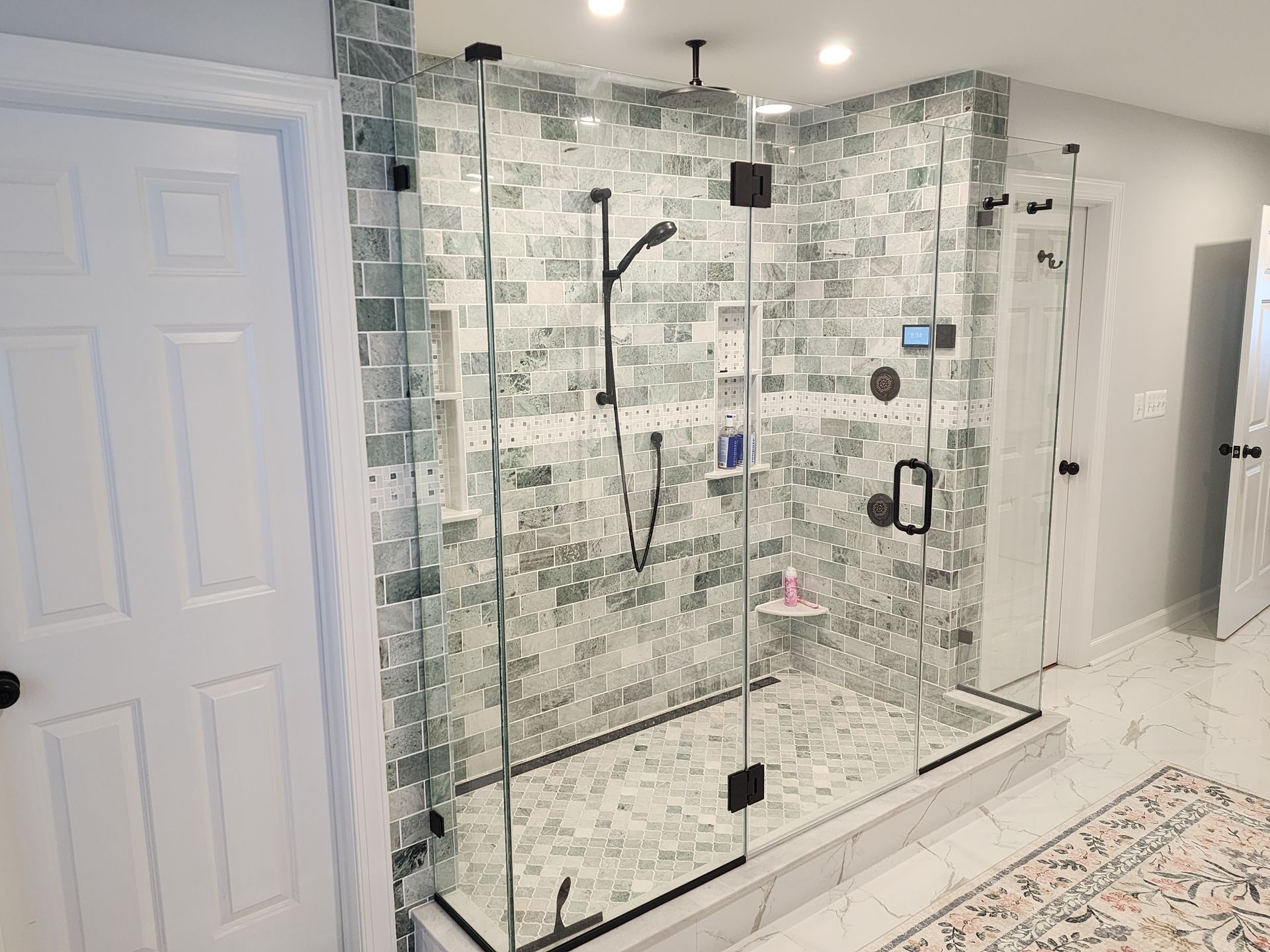 Modern bathroom with glass shower enclosure, mosaic tile, black fixtures, and white doors.