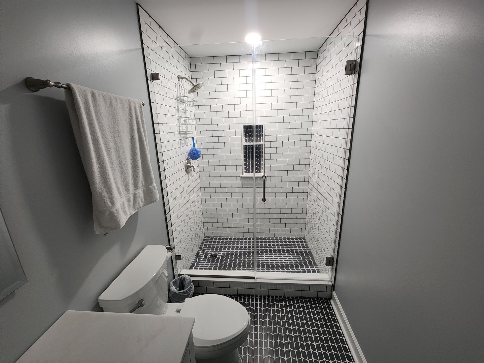 Small bathroom with white and black tiled shower, toilet, and towel rack.