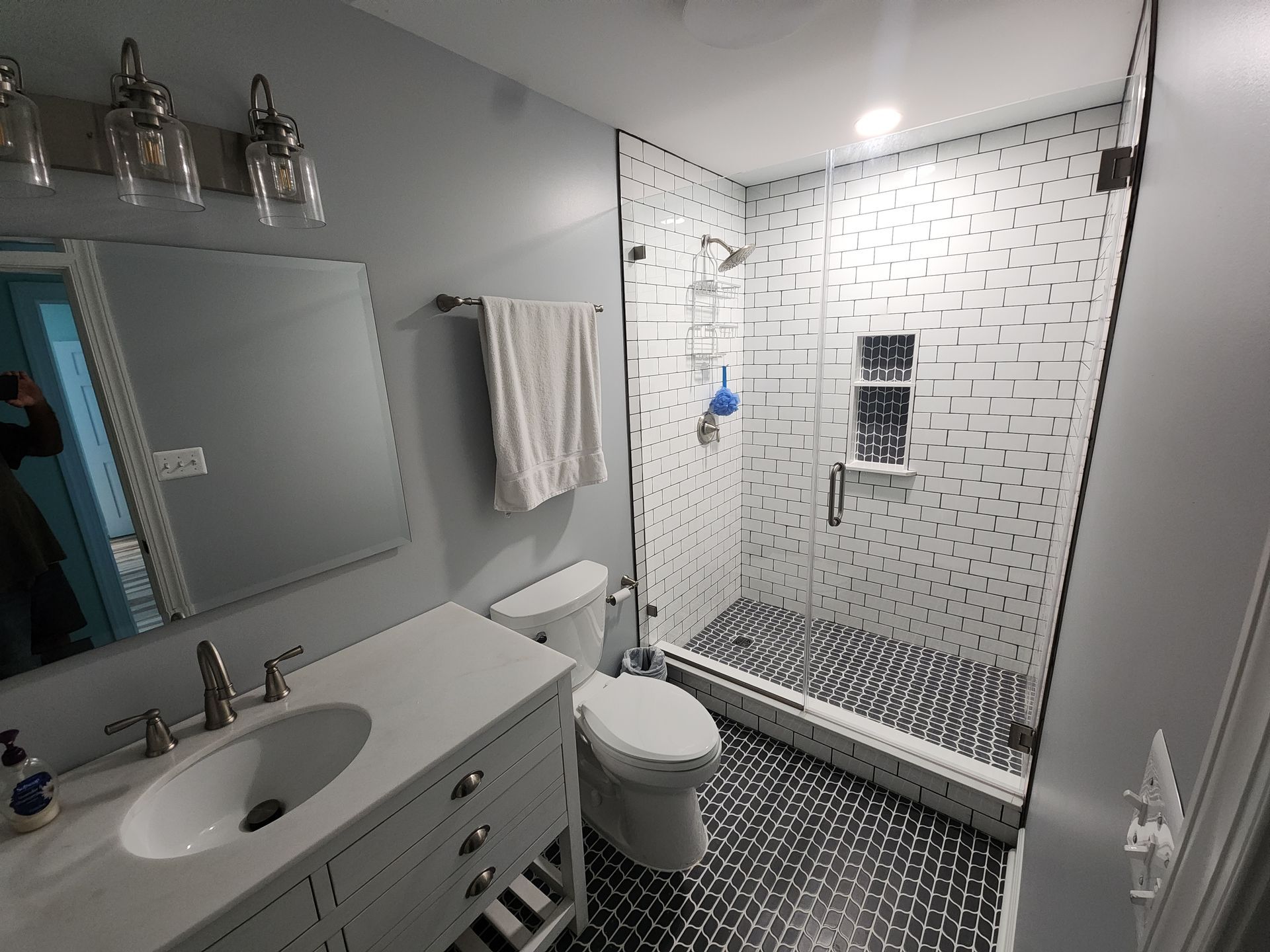 Bathroom with white vanity, toilet, and tiled shower. Light blue walls, gray and black floor.