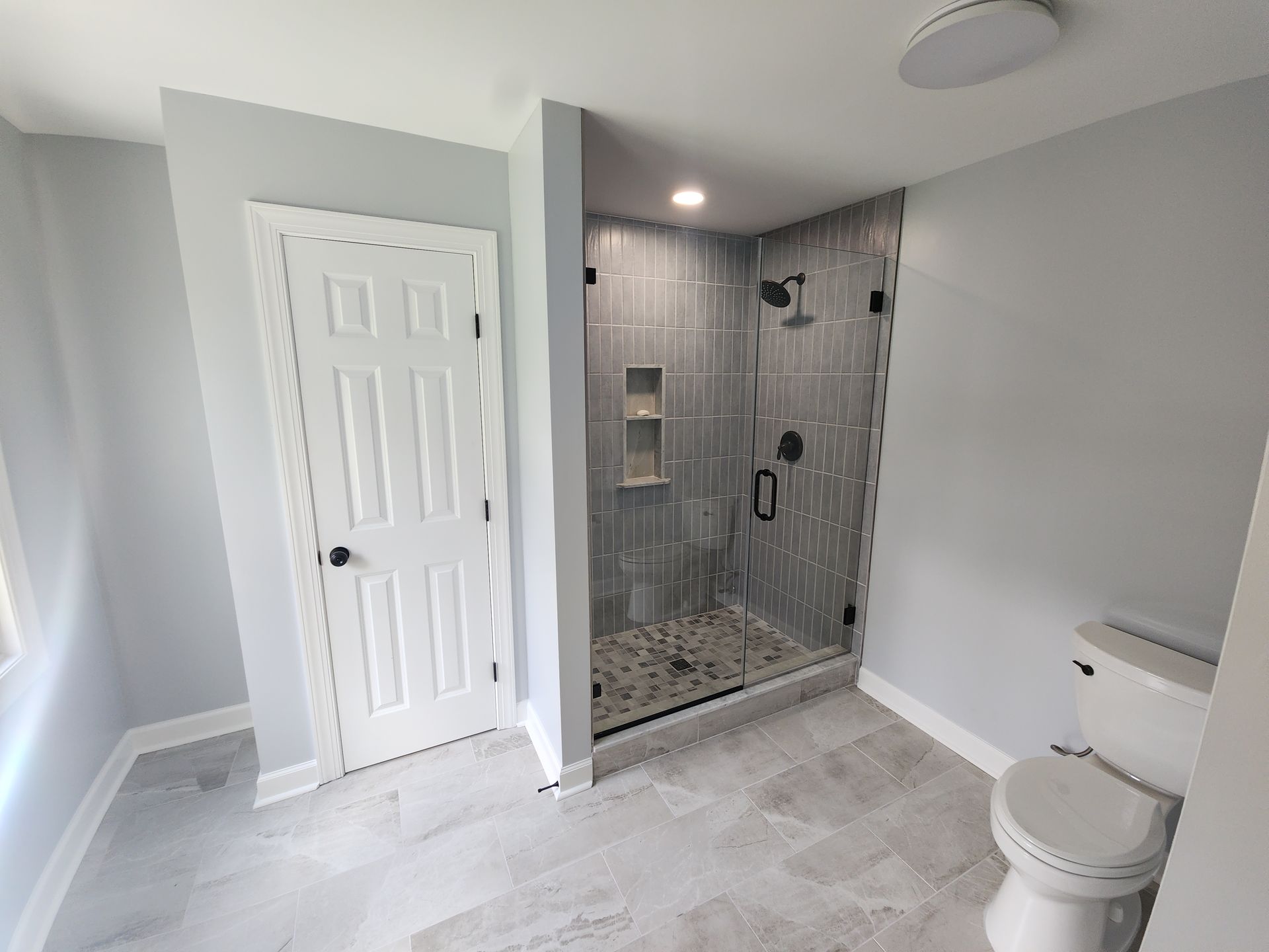 Newly renovated bathroom with gray tile floor, shower, and toilet; light blue walls, white door.
