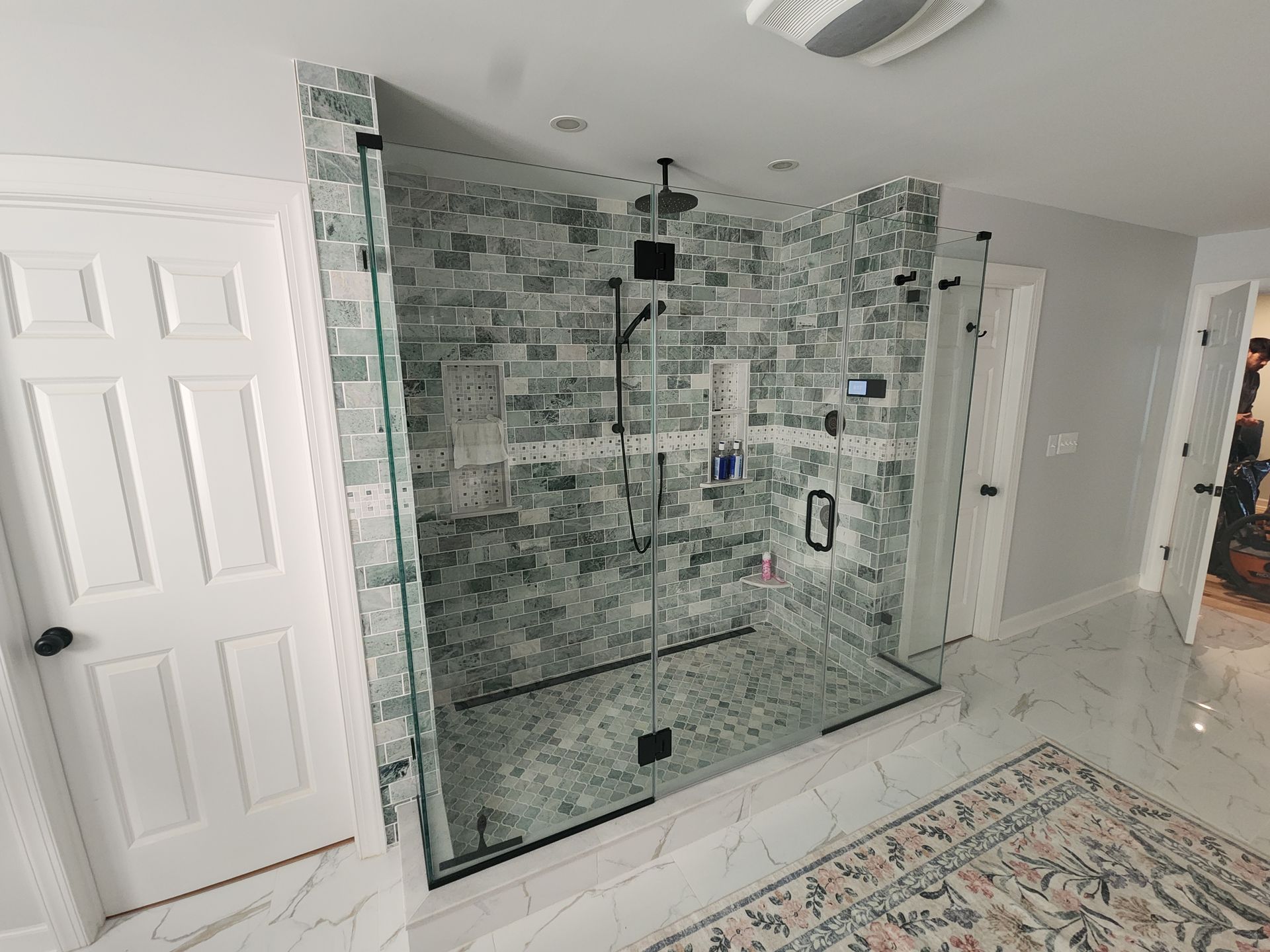 Modern bathroom with a large walk-in shower. Green tile wall, glass doors, and black fixtures.