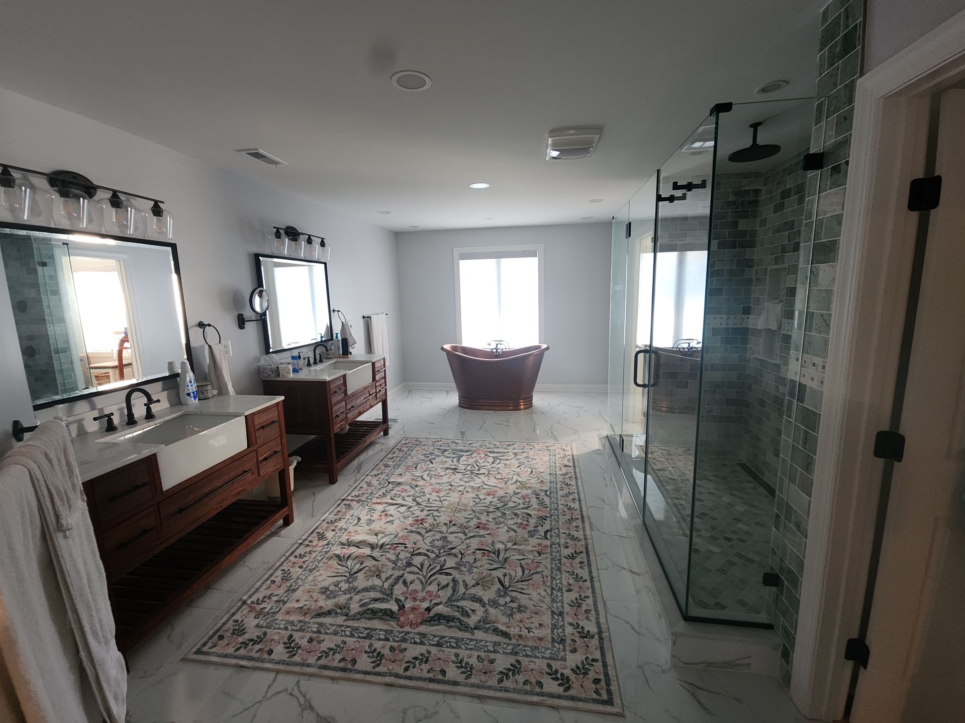 Spacious bathroom with a tub, two vanities, and a glass-enclosed shower on a patterned rug.