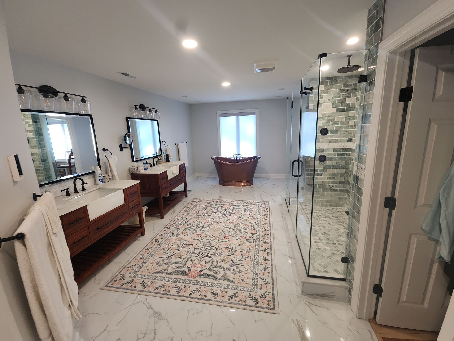 Spacious bathroom with wood vanities, a clawfoot tub, glass shower, and patterned rug.