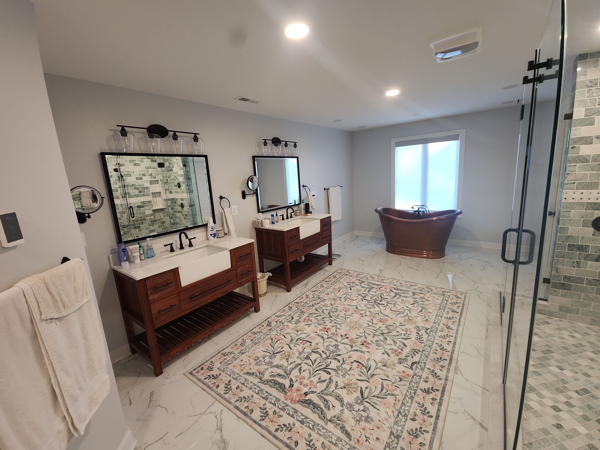 Spacious bathroom with two vanities, a free-standing tub, and a decorative rug on a tiled floor.