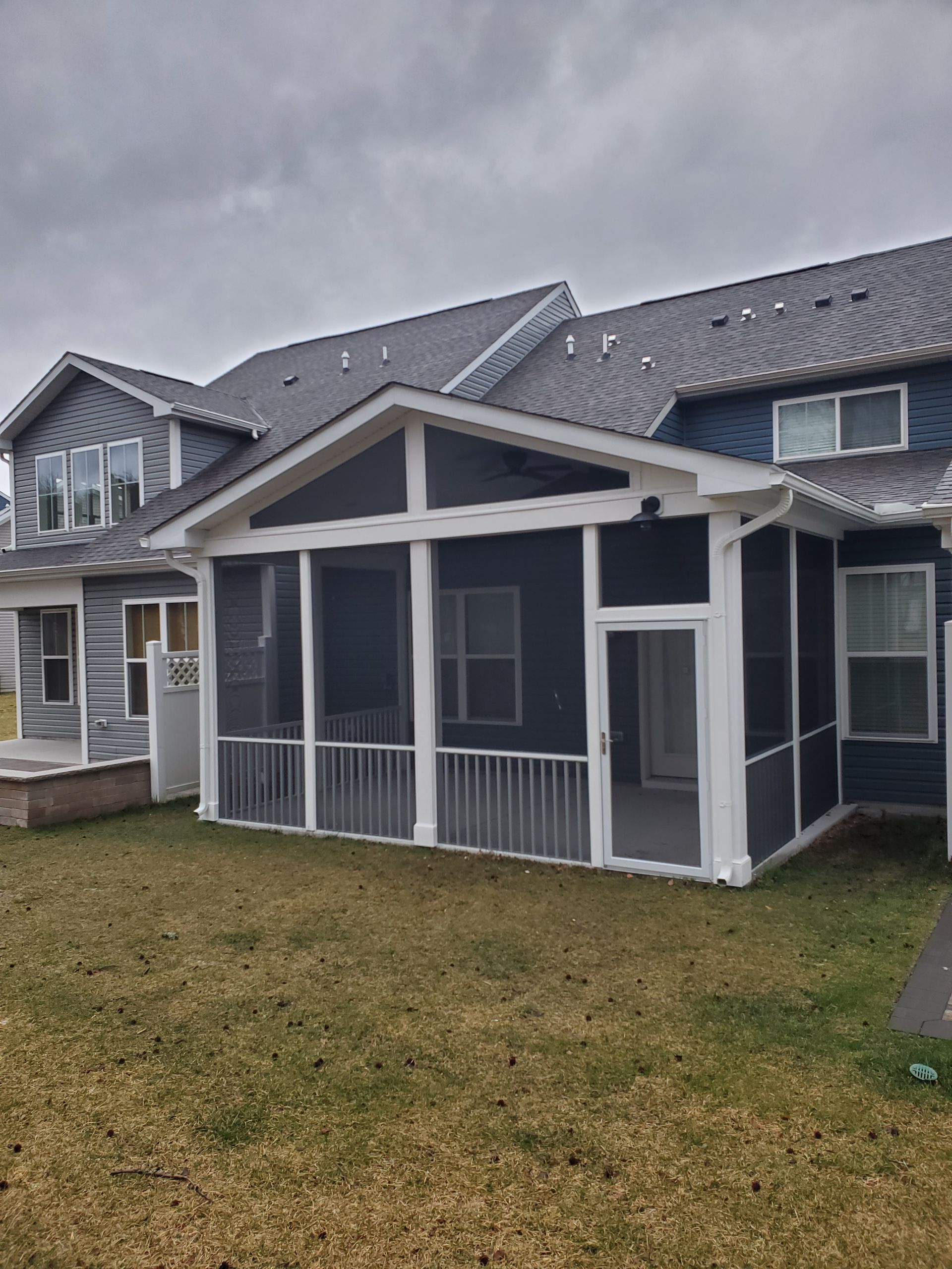 Screened-in porch attached to a blue house with white trim. The porch has a peaked roof and is on a grassy lawn.