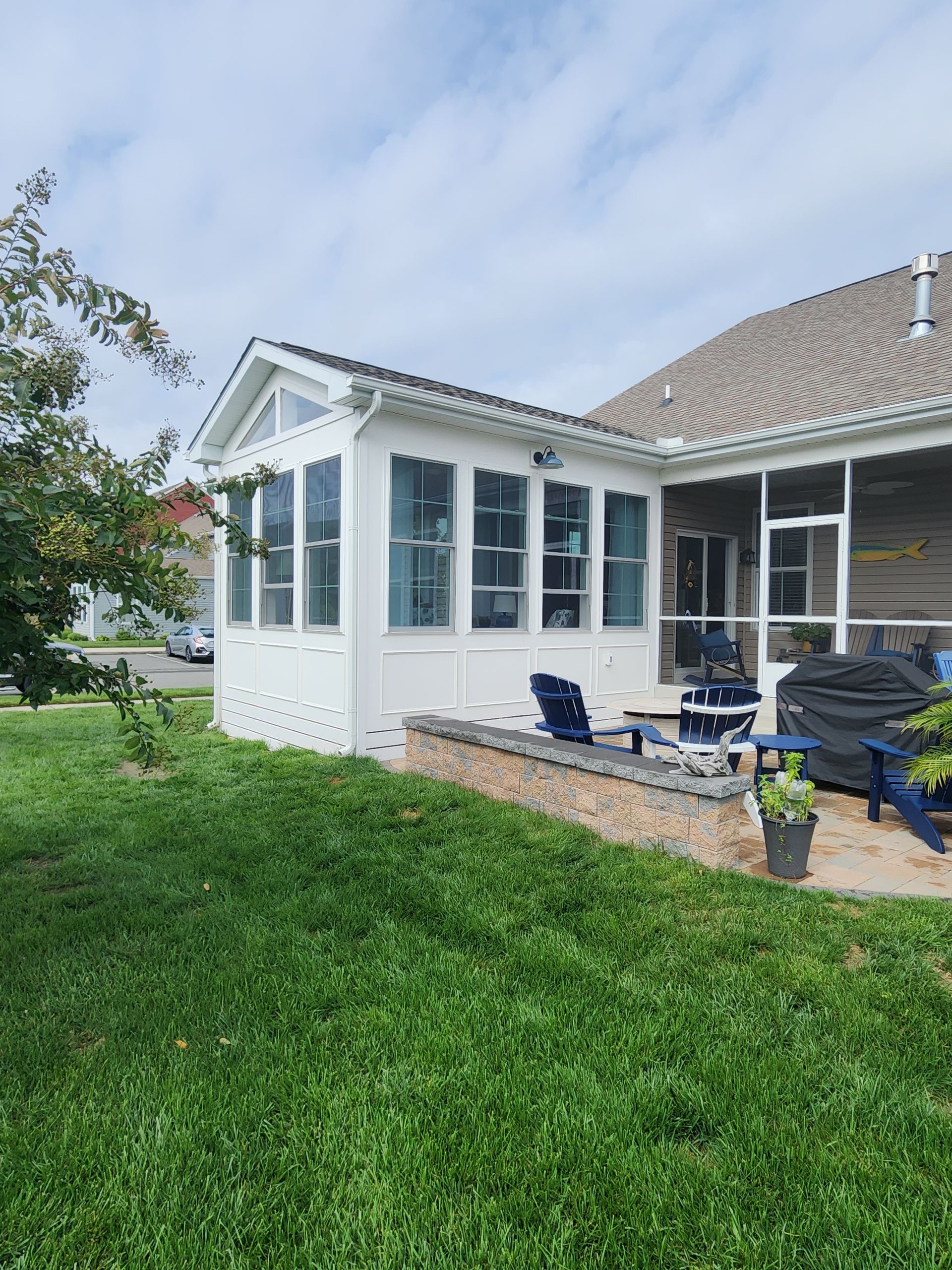 White screened-in porch next to a house with an attached patio area on a sunny day.