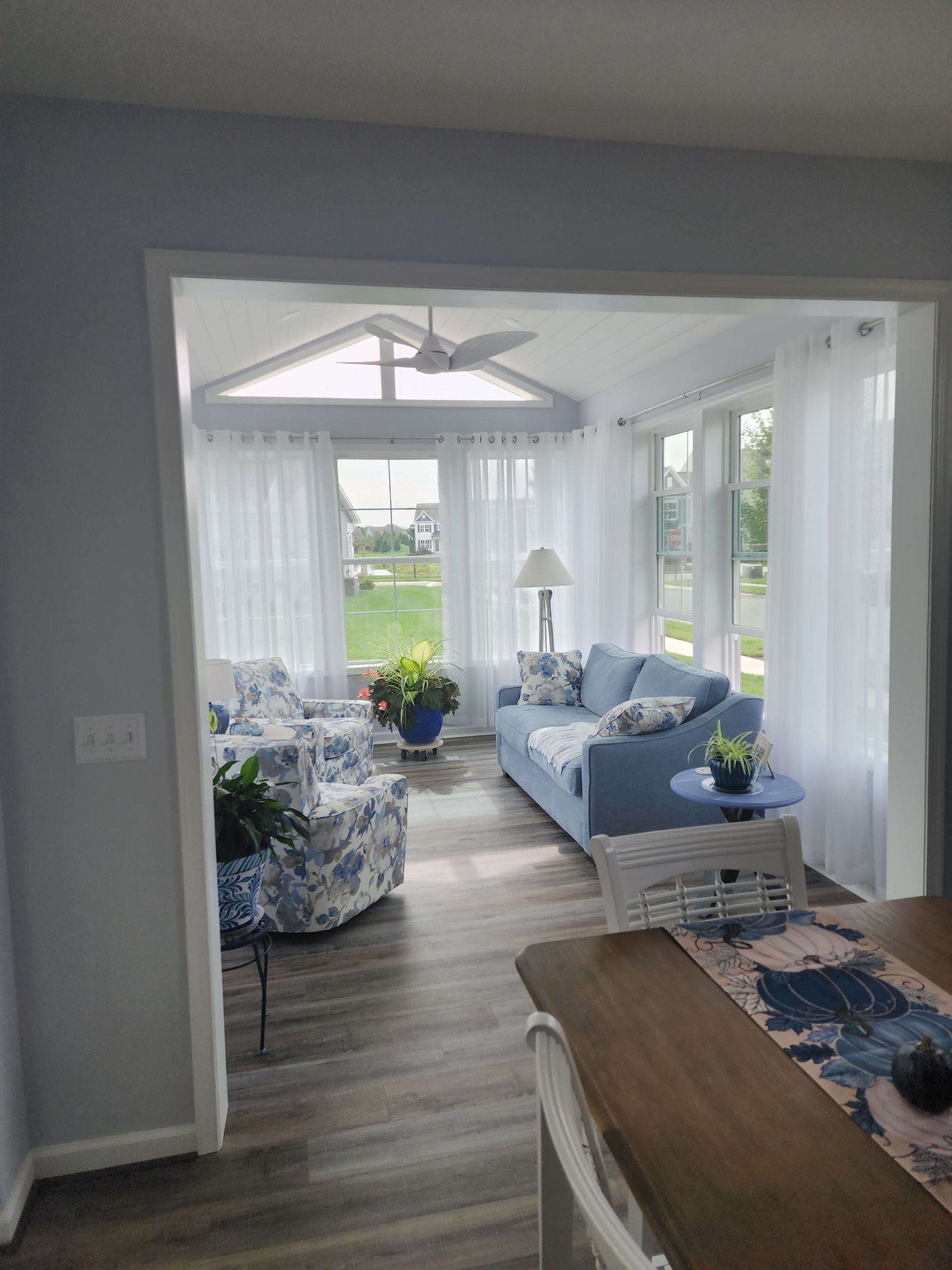Blue and white sunroom with light blue furniture, white curtains, and a view to the outside.