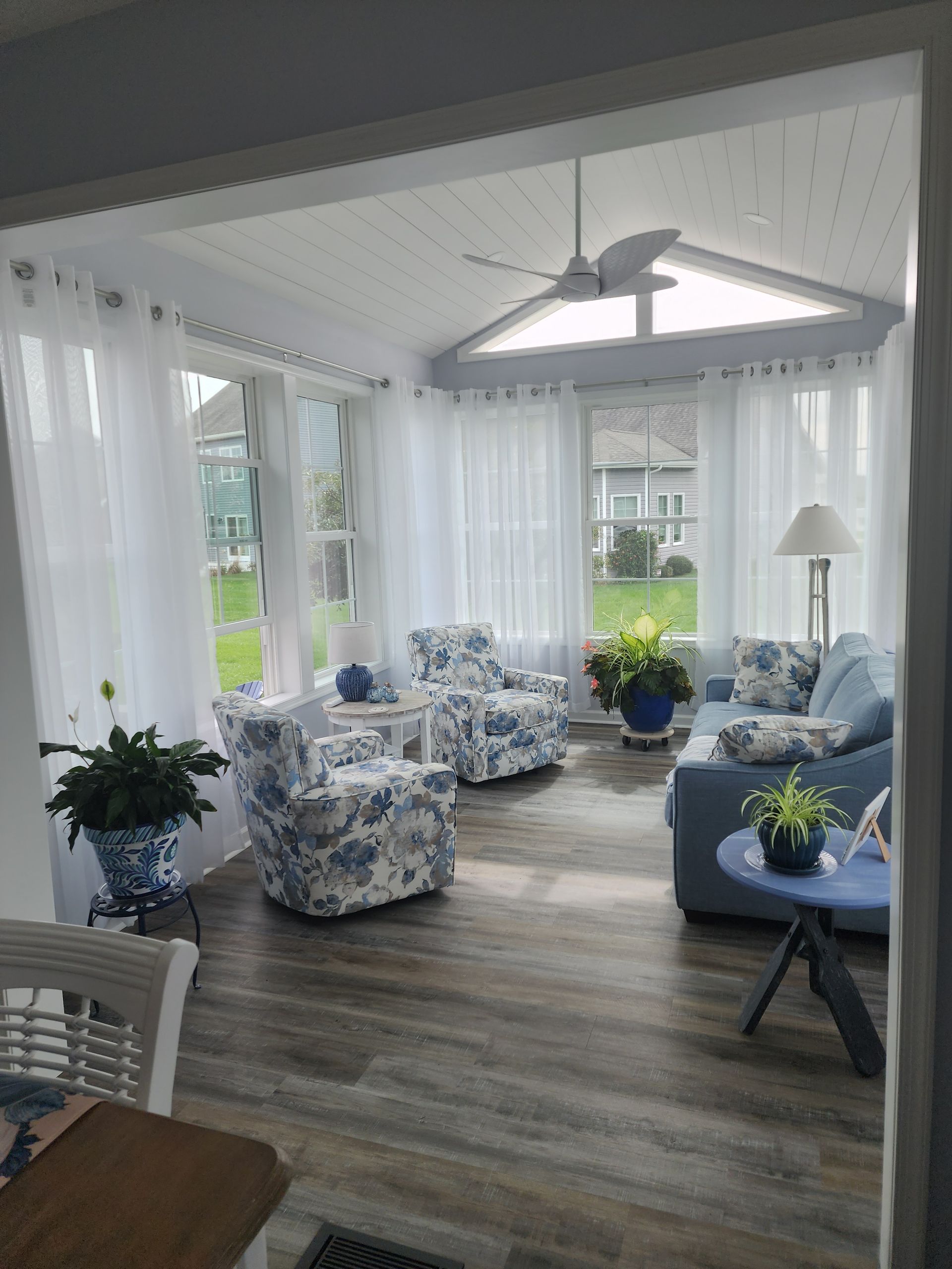 Sunroom with blue and white floral furniture, sheer white curtains, and a ceiling fan.