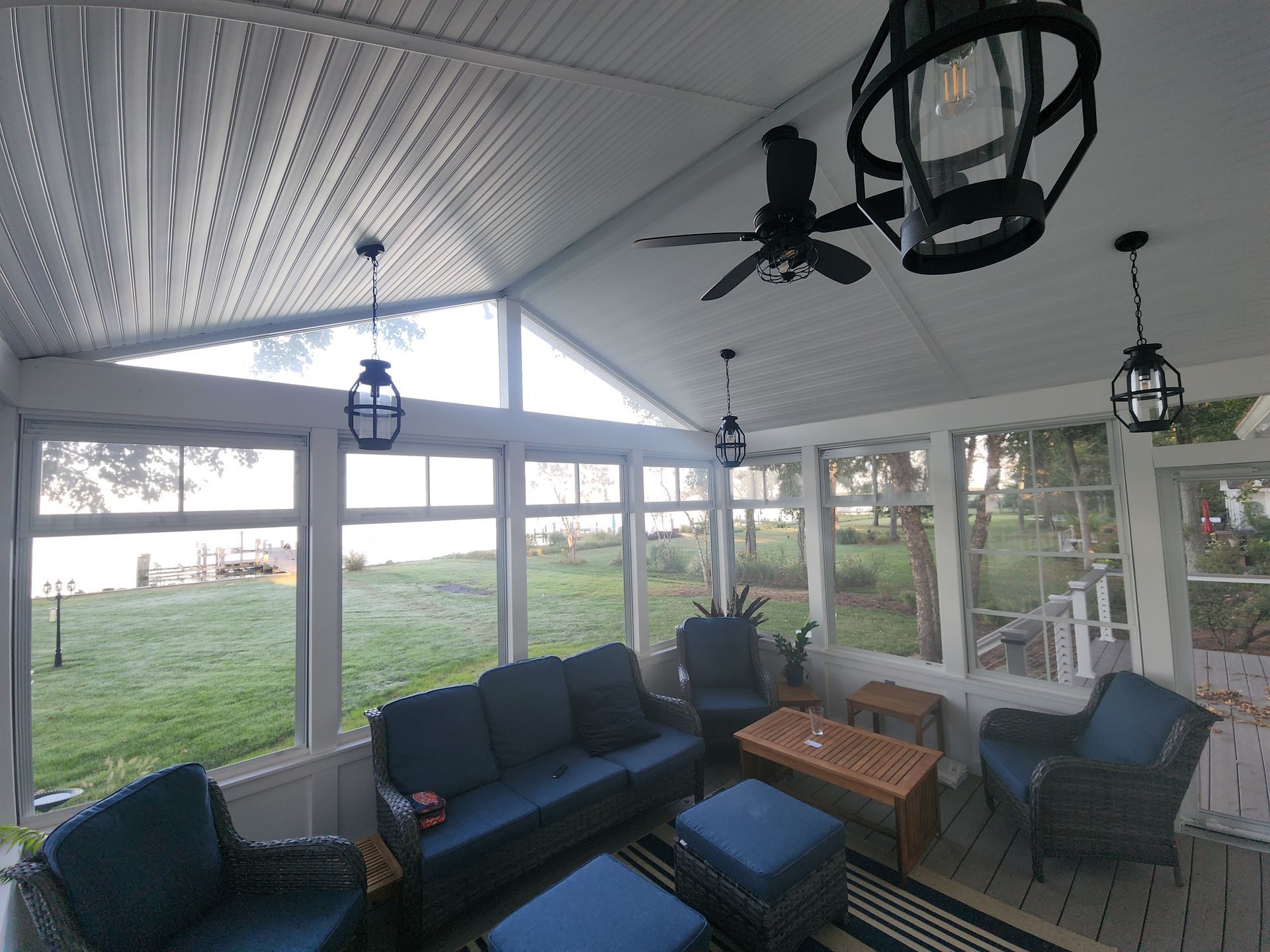 Sunroom with blue furniture, black light fixtures, and a view of a grassy area and water.