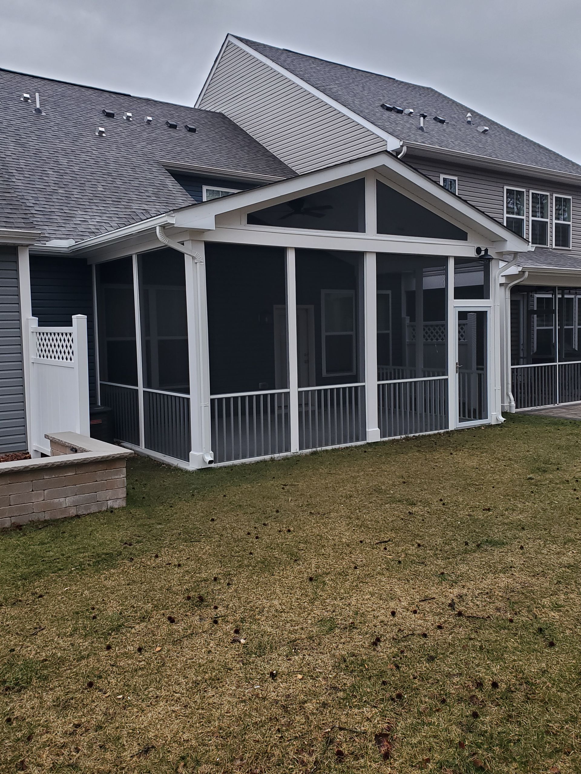 Screened-in porch attached to a house with white trim, gray roof and siding, and a small patch of grass.